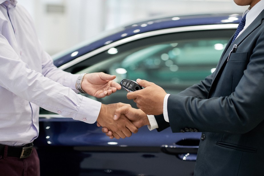Salesman giving car keys to customer who has chosen a new car and shaking his hand