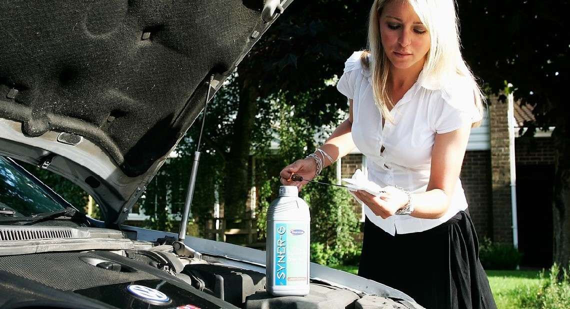 Woman leans over her car as she checks the oil.