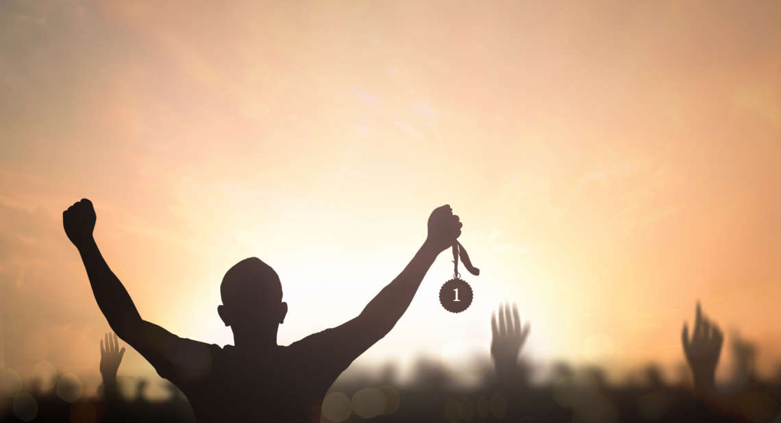 Silhouette winner hand holding gold medal reward against blurred sport stadium sunset background
