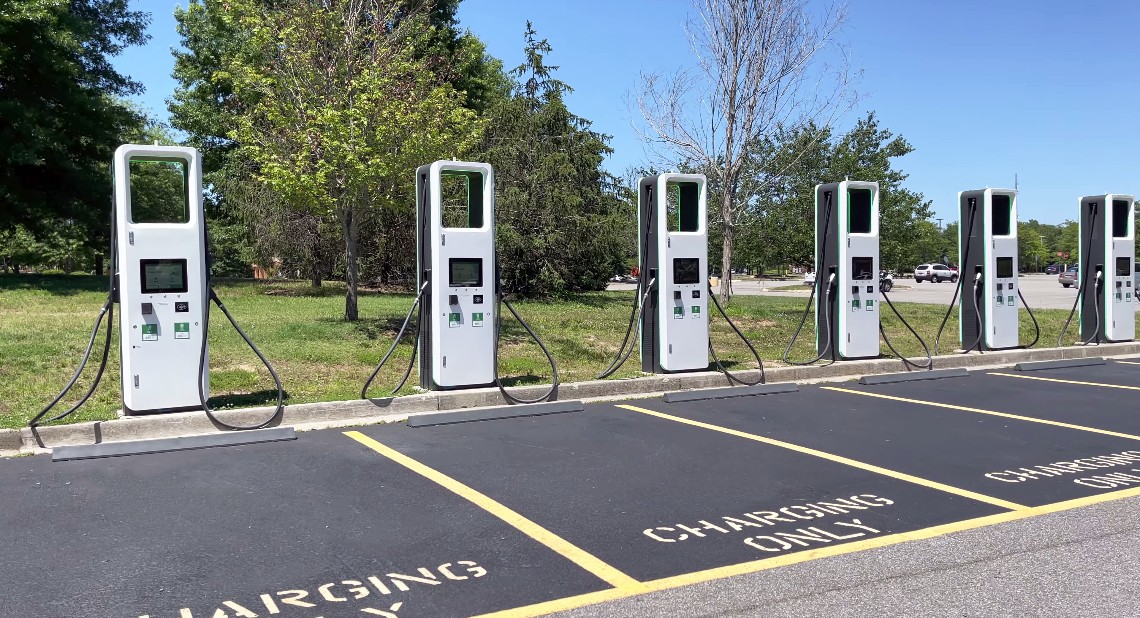 electric charging station with many electric chargers and a parking lot on a sunny day.