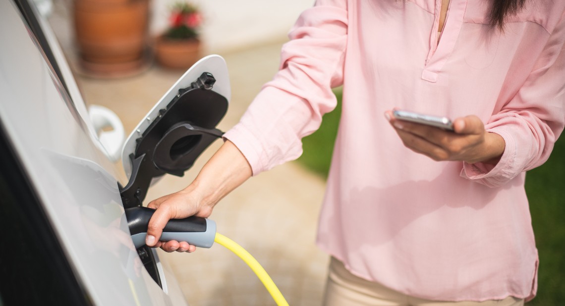 Woman charging electric car and making time adjustment on a smartphone