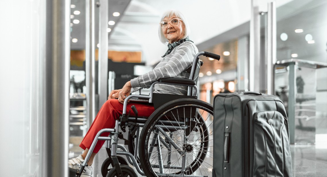 Image of a mature female with a suitcase sitting in a wheelchair at the airport