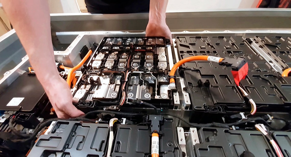 close-up of a mechanic's hands disassembling an electric car battery inside a mechanic shop