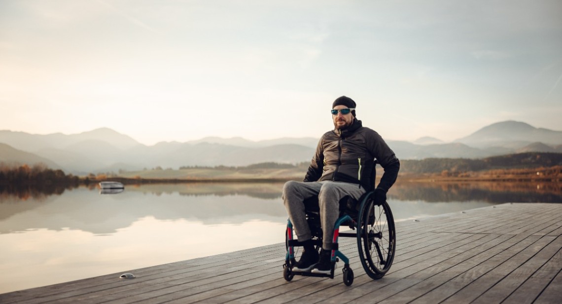 wheelchair user tourist on wooden pier with lake and mountain in the background during winter