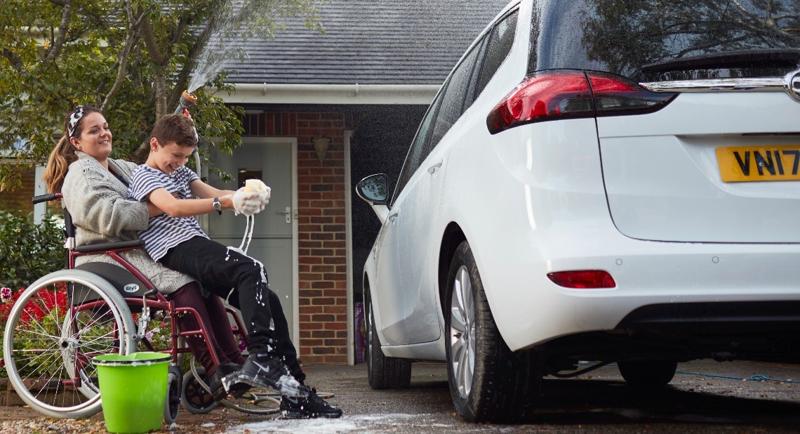 Woman in wheelchair holding her son while they are cleaning the car