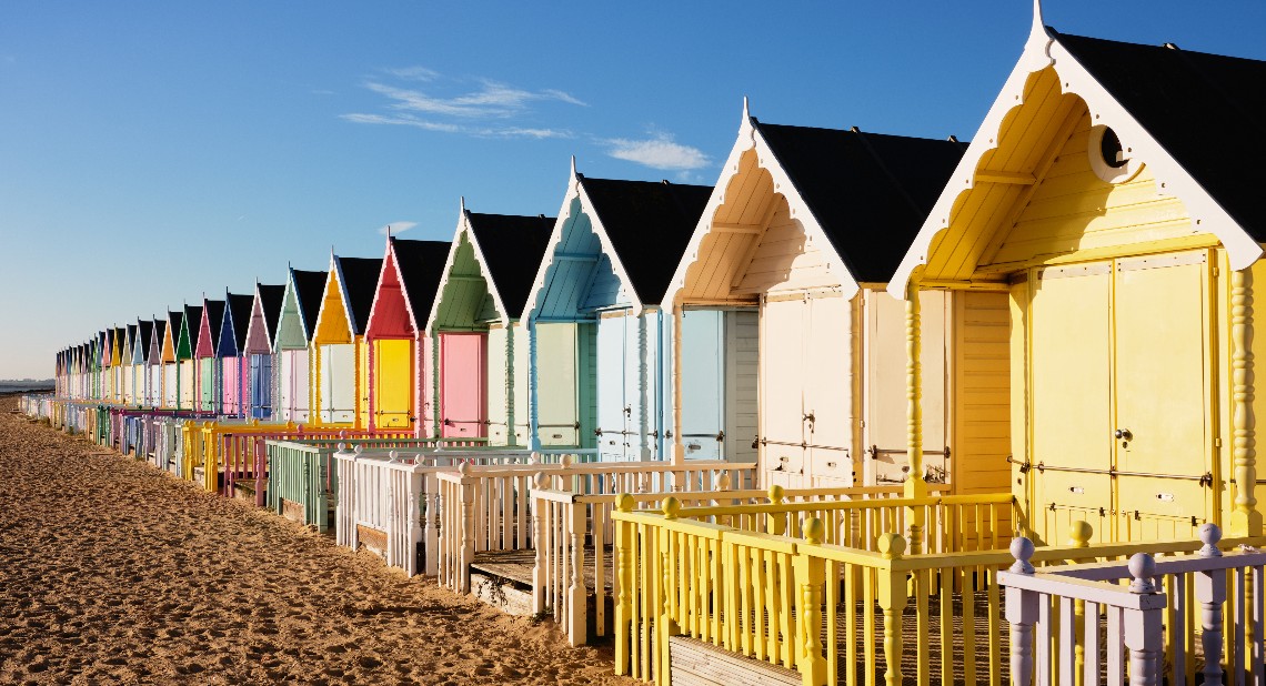 UK, Essex, Mersea Island, row of multi coloured beach huts in bright sunshine