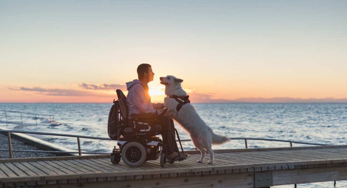 A man and his dog on a beach with the sun setting behind them.