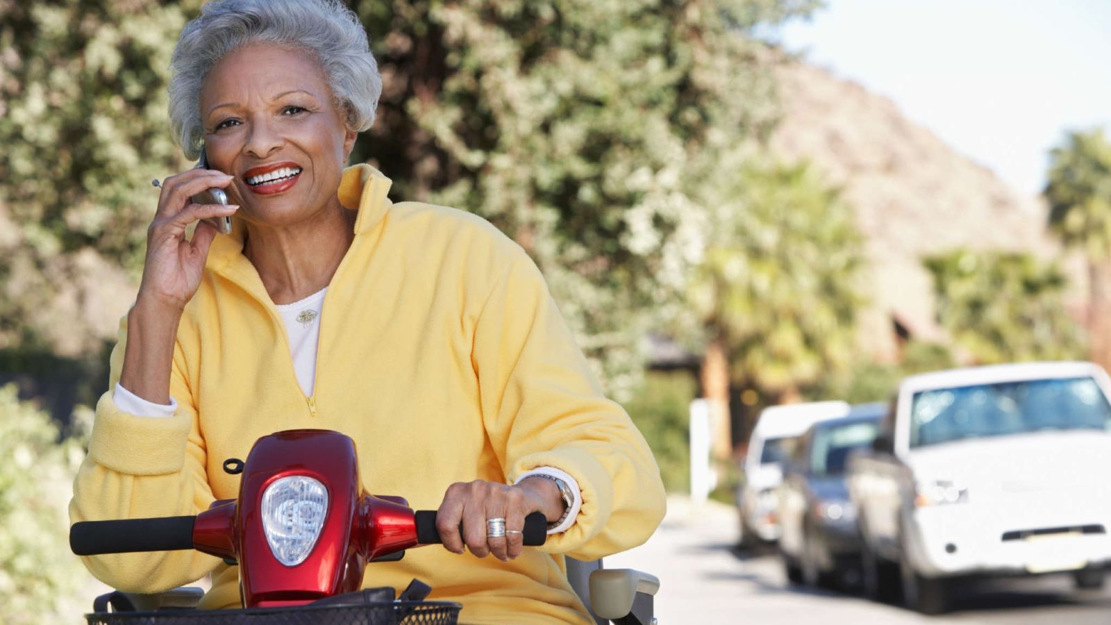 An elder woman on a wheelchair going down a suburban street