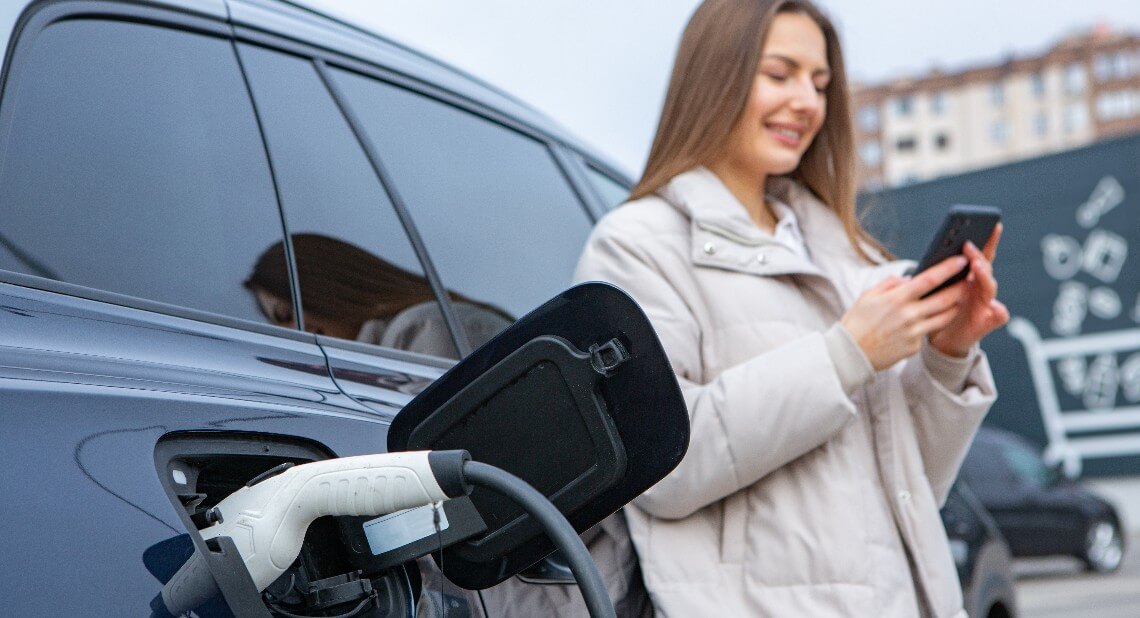 Young woman using an app on her phone to charge her electric vehicle in public.