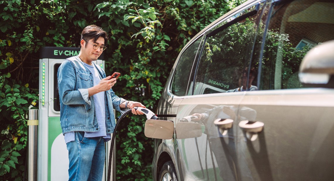 Man charging his EV and using his phone