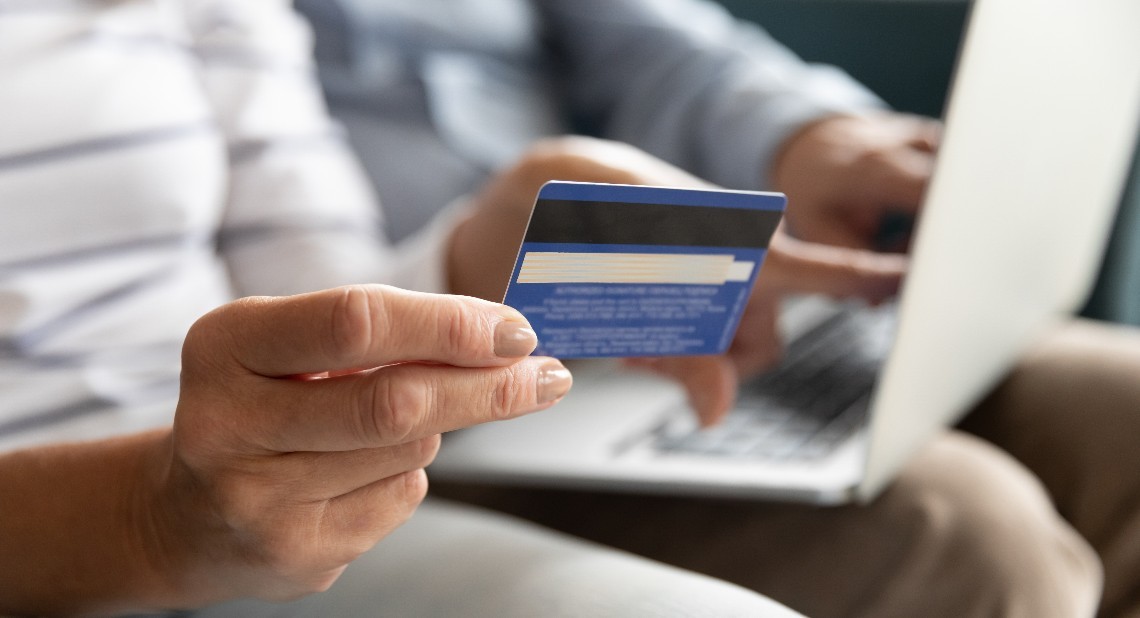 Someone holding a bank card with a laptop in the background