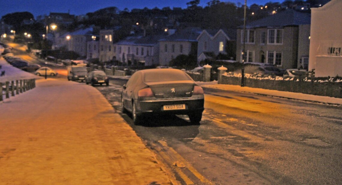 A snowy street with cars parked