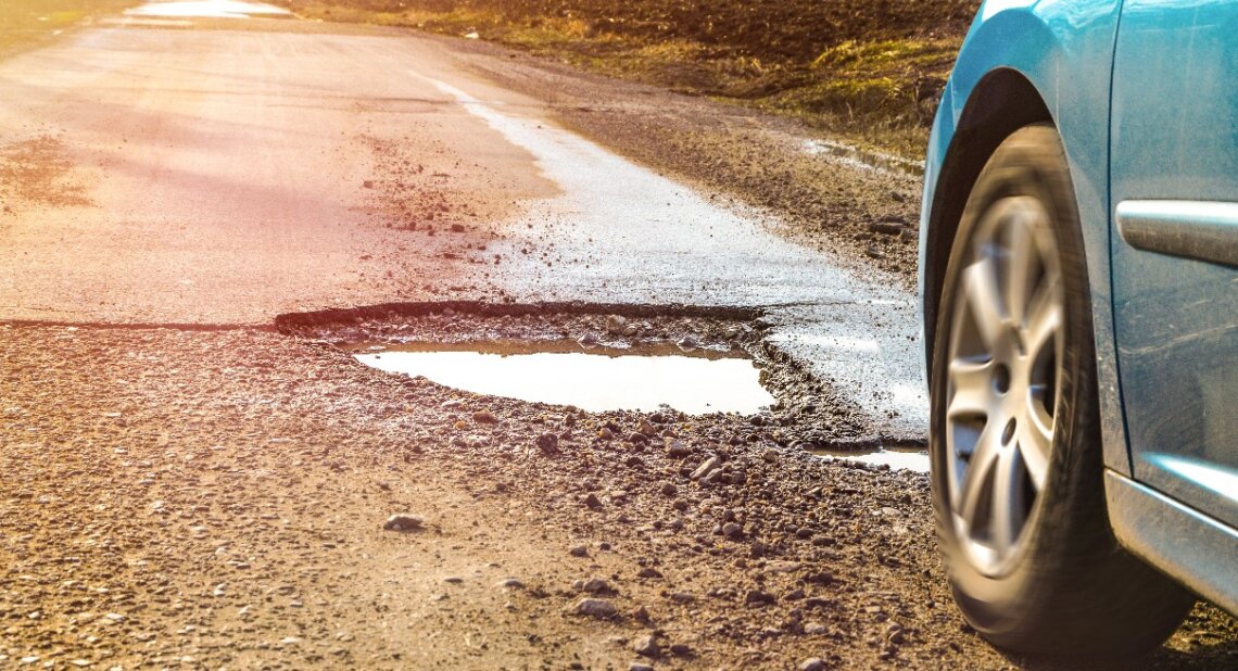 a pothole on a road featuring a car wheel