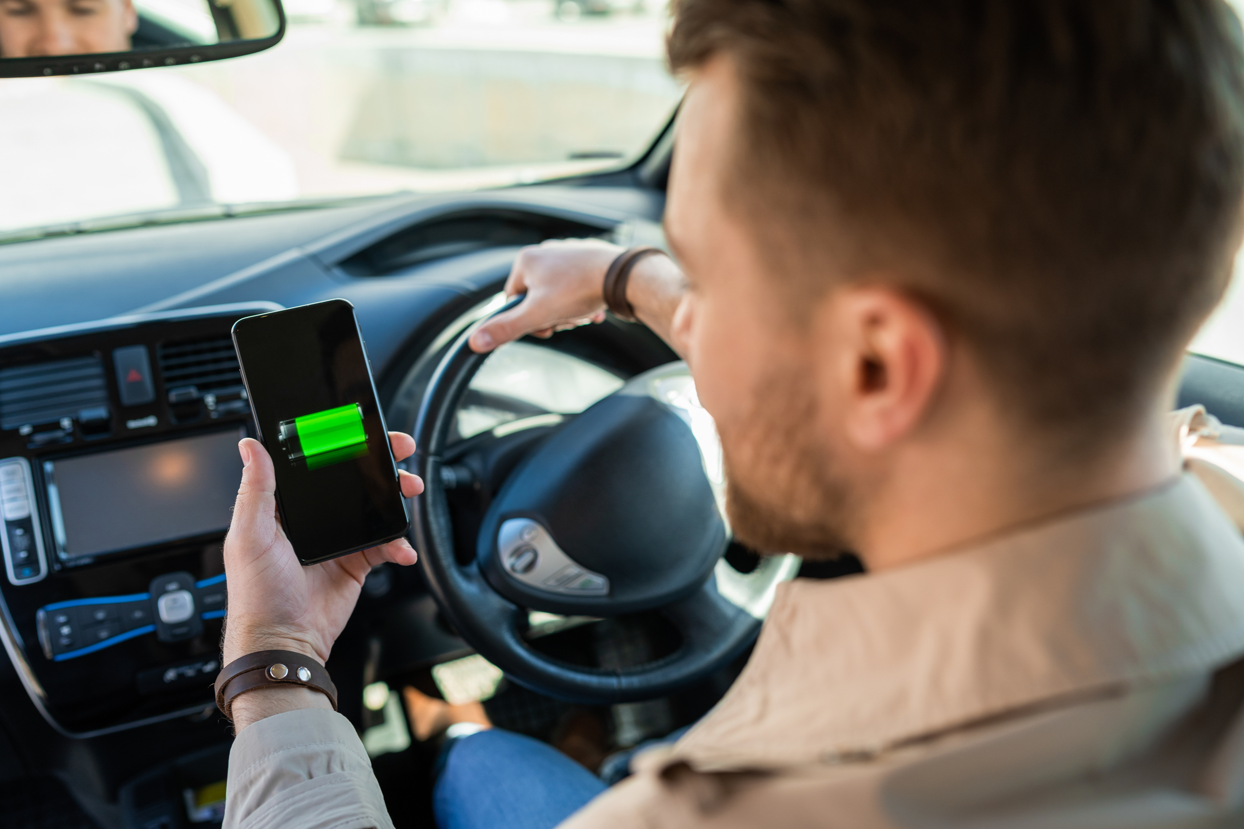 Man watching electric car charge indicator through smartphone app. Battery level on the mobile phone screen