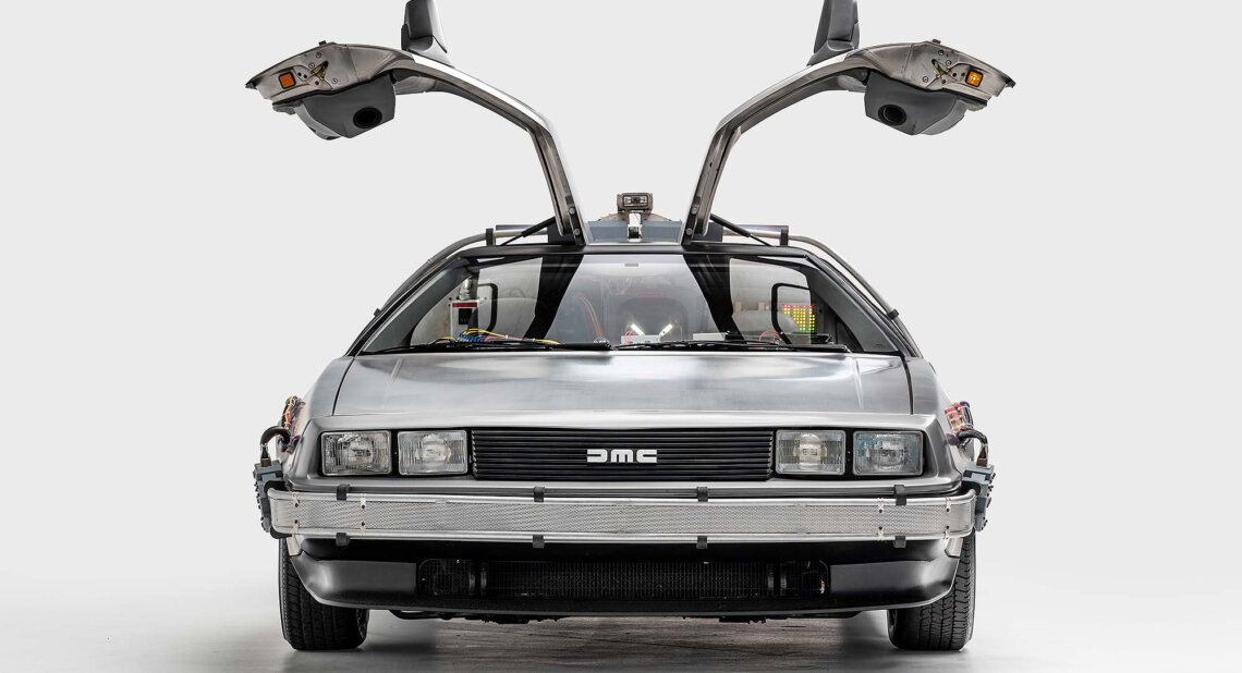 A modified DeLorean DMC-12 from the Back to the Future film, shown head-on with gullwing doors open and time-travel electronics visible inside and on the bumper.