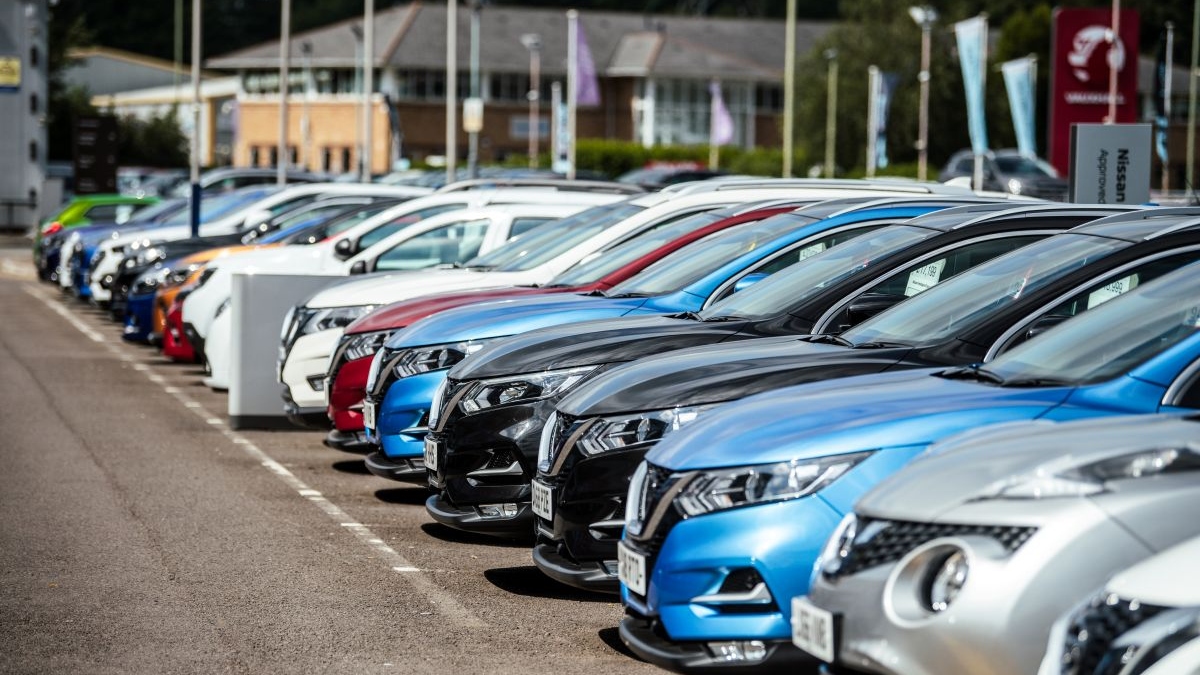 A row of cars parked outside a dealership. The vehicles are lined up neatly, with the dealership sign just visible.