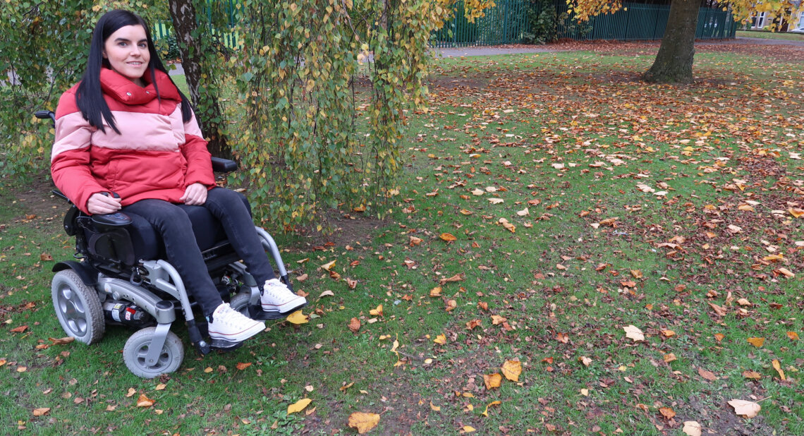 Emma Muldoon is sat outdoors in her powered wheelchair.