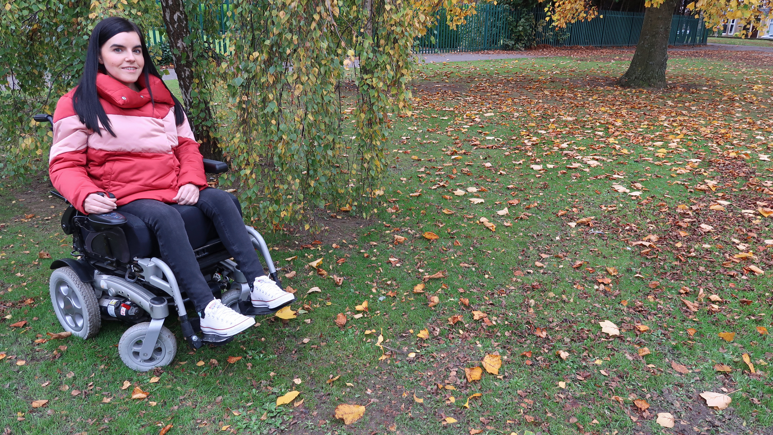 Emma Muldoon is sat outdoors in her powered wheelchair.