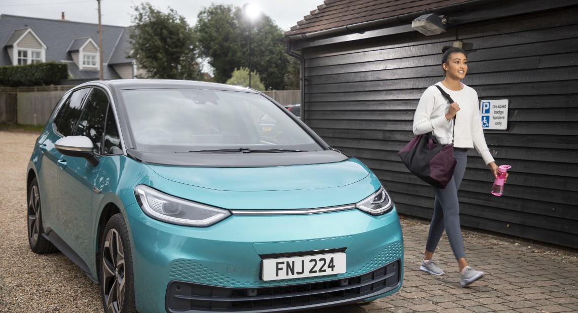 smiling women in gym clothes walking next to her Motability Scheme car