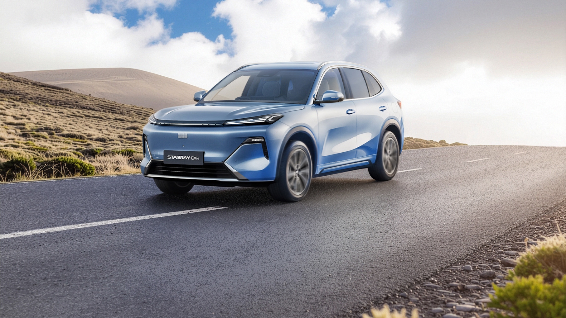 Light blue Geely Starray SUV driving along an open road through a hilly landscape under a bright sky with scattered clouds. The vehicle is shown in three quarter front view, with motion blur on the wheels and road surface to suggest movement.