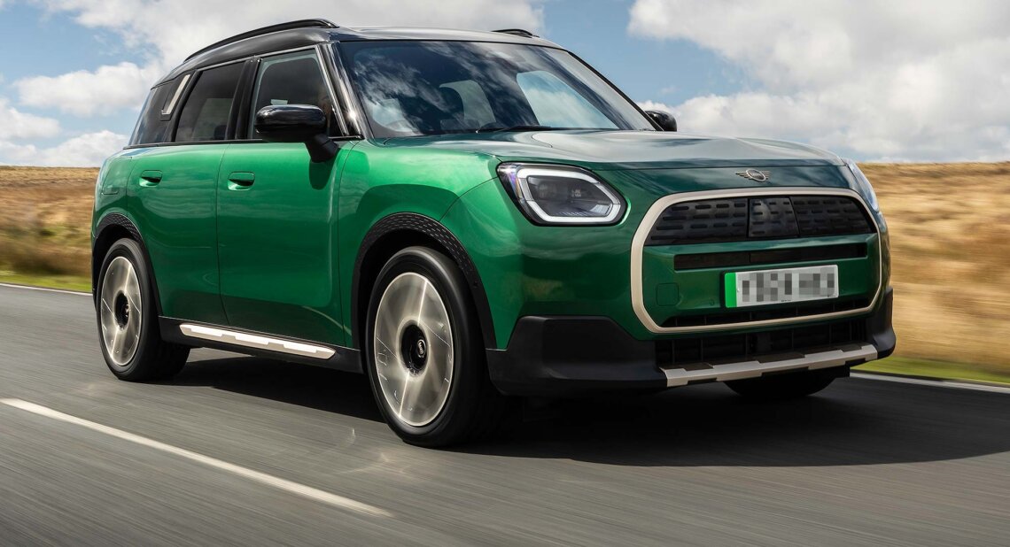 Green MINI Countryman SUV driving along a winding rural road with hills in the background, available on the Motability Scheme with no Advance Payment.