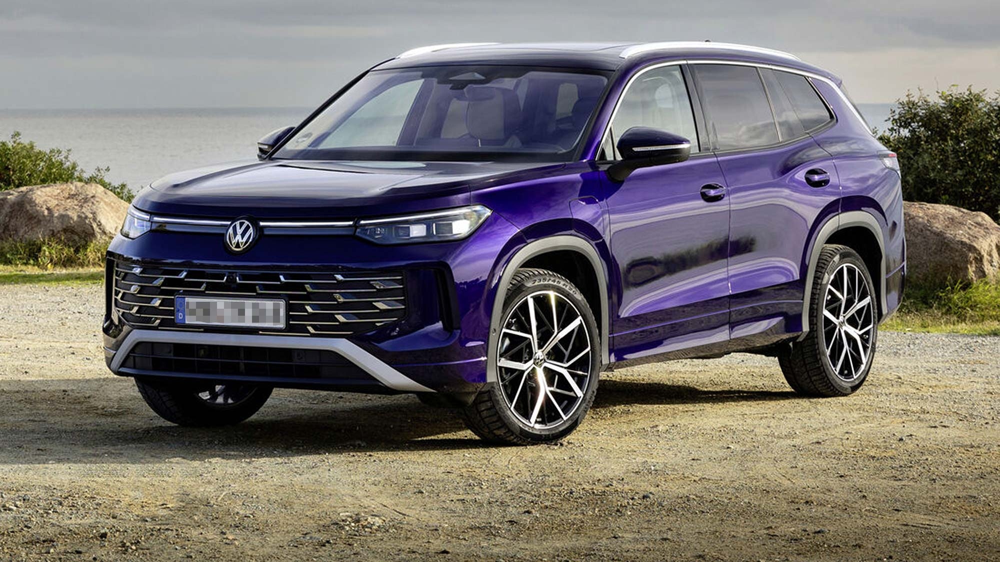 A purple Volkswagen Tayron SUV parked near a coastal setting with rocks and sea behind, front three quarter view, available on the Motability Scheme.