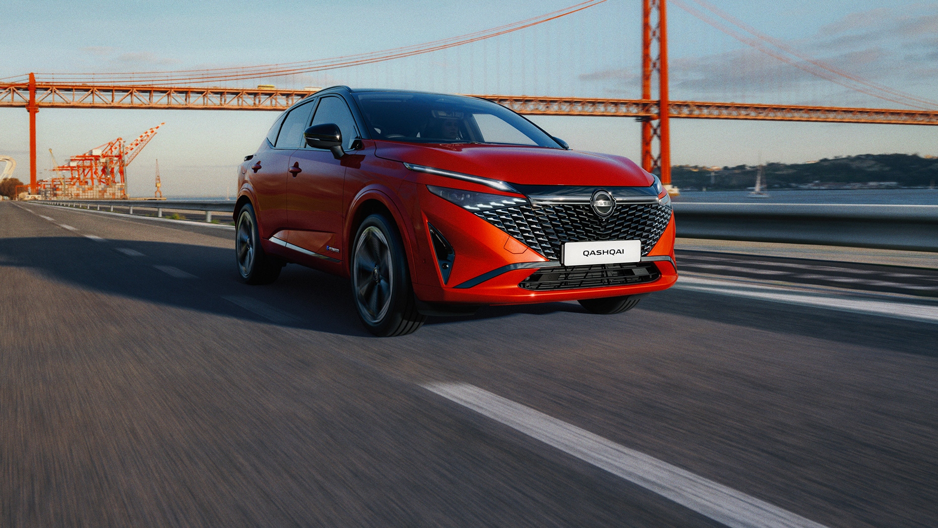 Red Nissan Qashqai driving on a road across a bridge, with industrial cranes and water in the background.