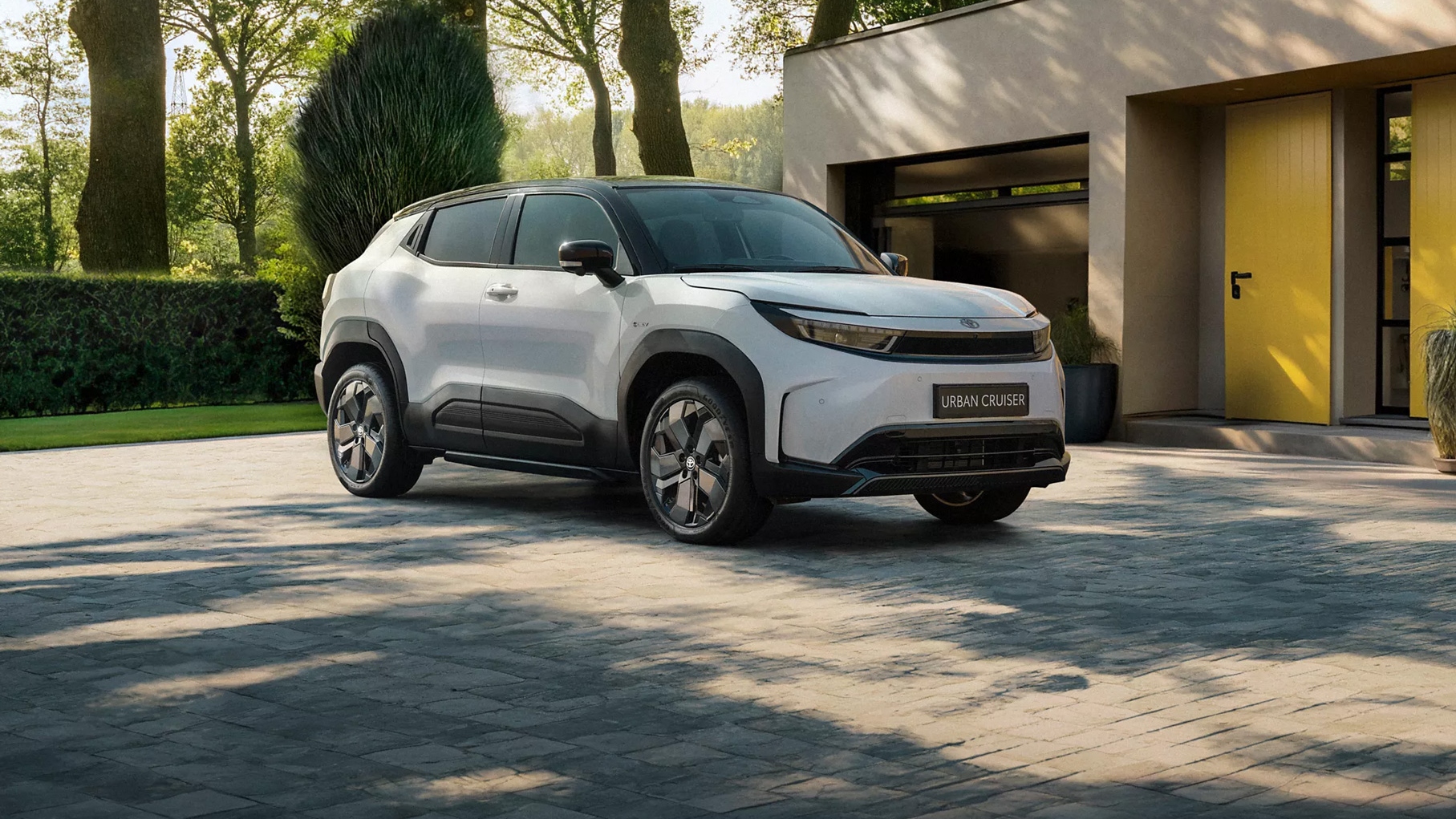 White Toyota Urban Cruiser parked on a driveway outside a modern house, with trees and greenery in the background.