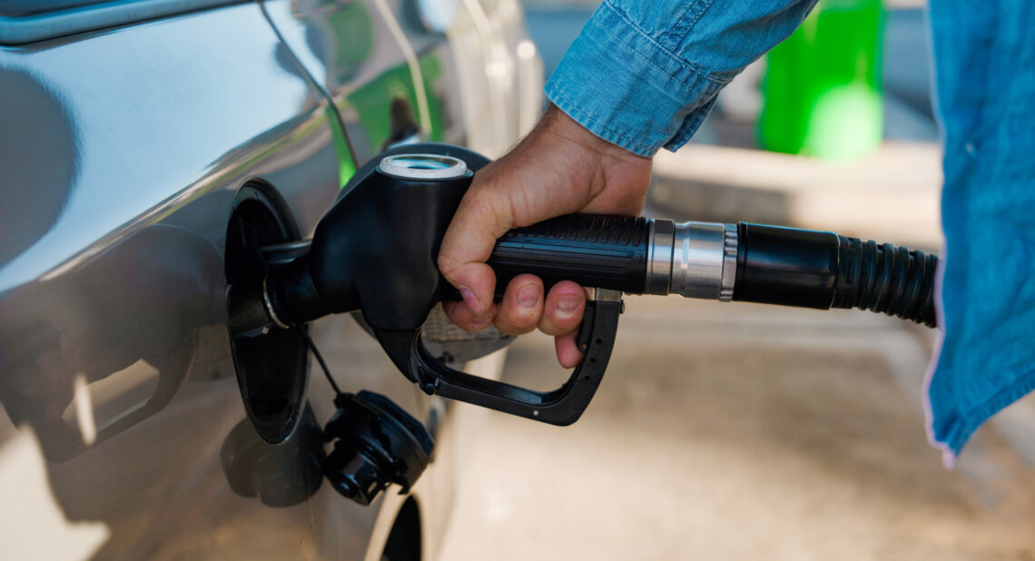 A driver filling a car with fuel at a petrol station, holding the nozzle in the fuel tank.