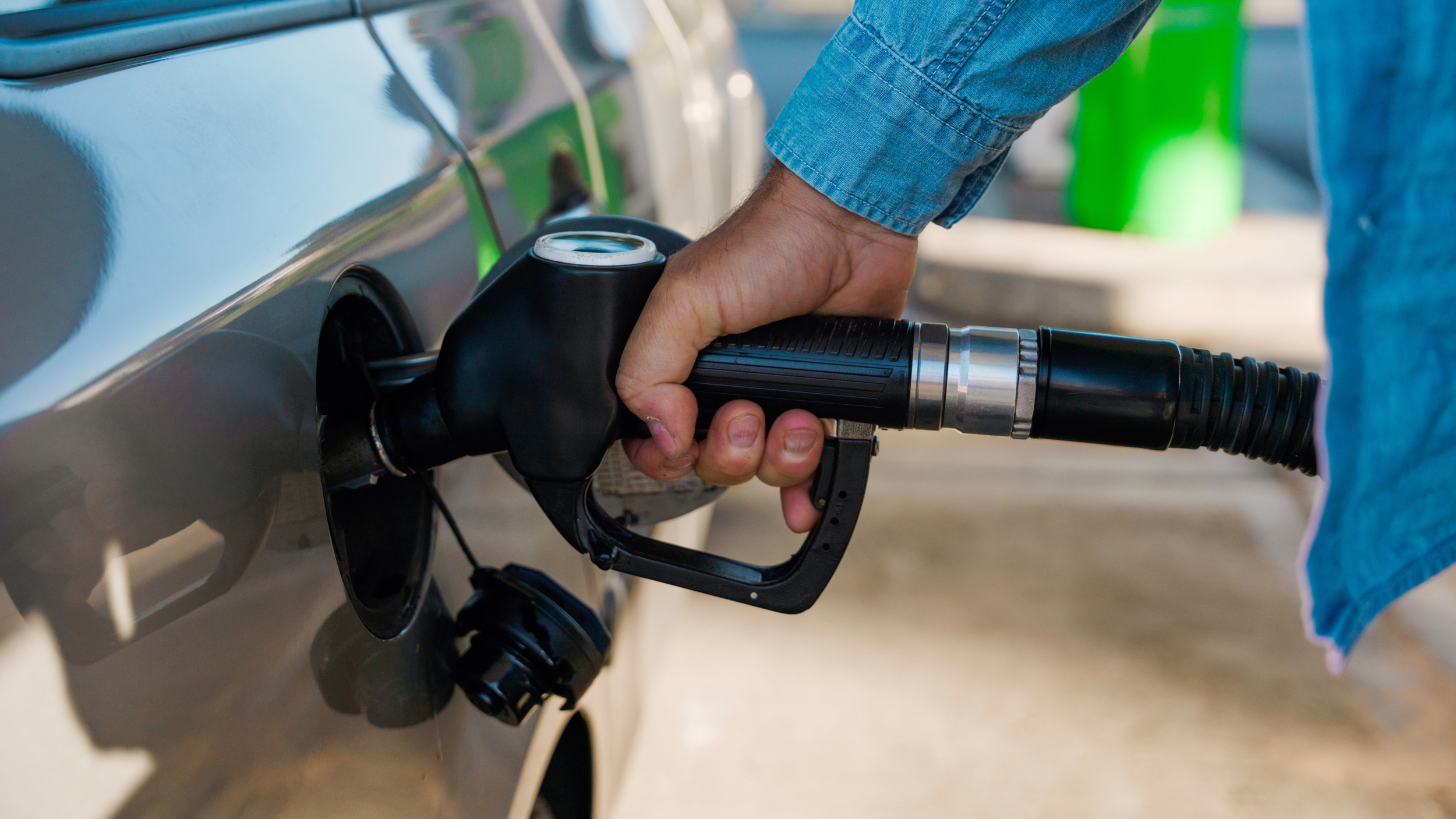 A driver filling a car with fuel at a petrol station, holding the nozzle in the fuel tank.