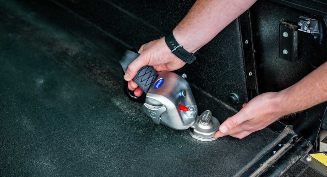 Hands securing a wheelchair restraint inside a Wheelchair Accessible Vehicle (WAV).