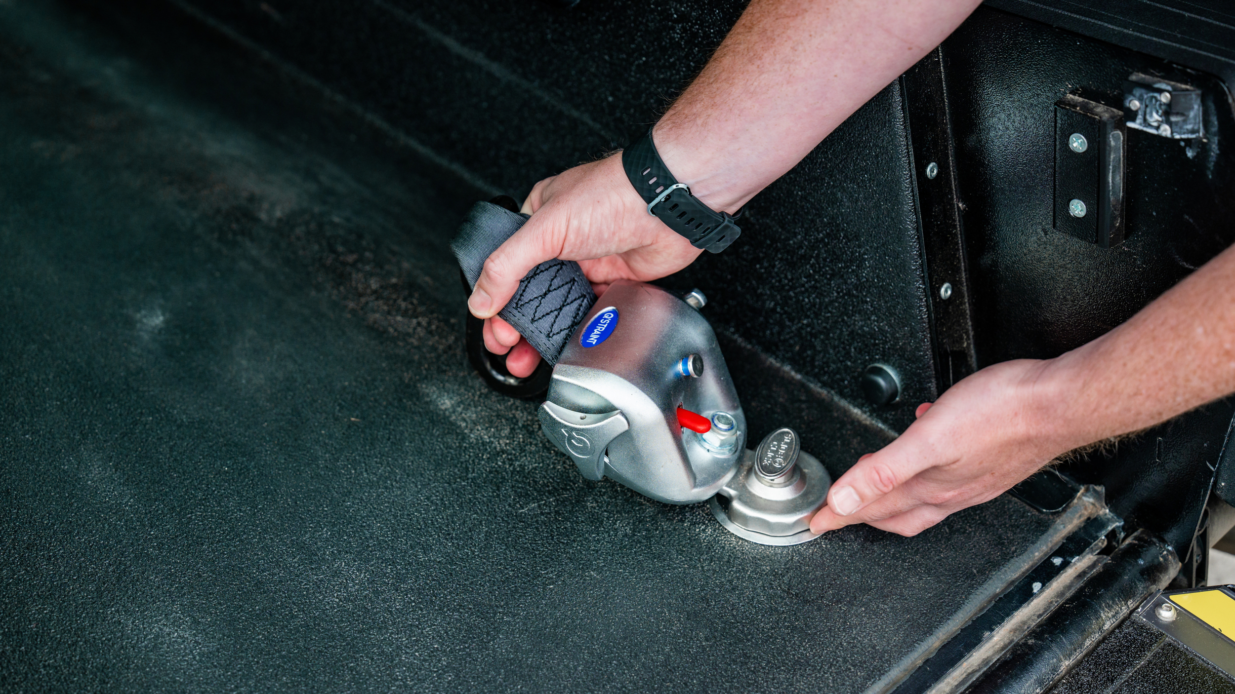 Hands securing a wheelchair restraint inside a Wheelchair Accessible Vehicle (WAV).