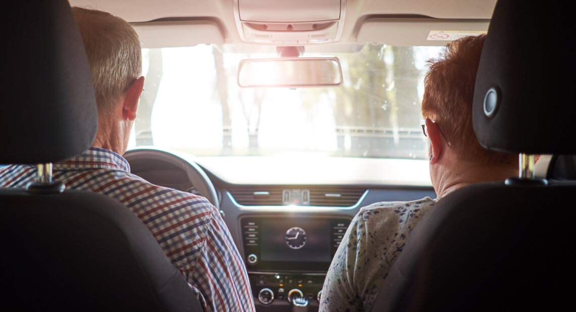 Senior couple driving car during road trip. View from back.