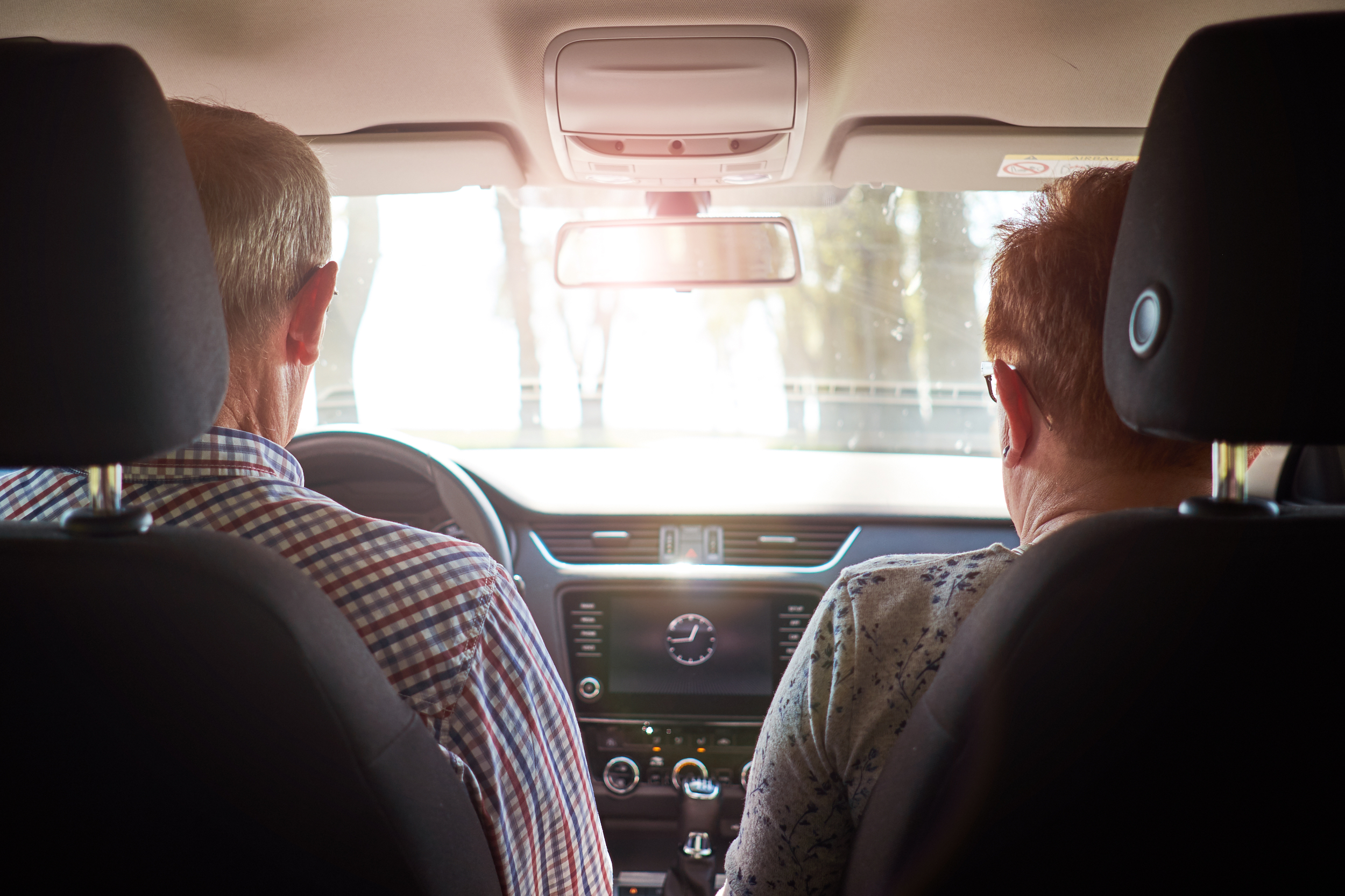 Senior couple driving car during road trip. View from back.